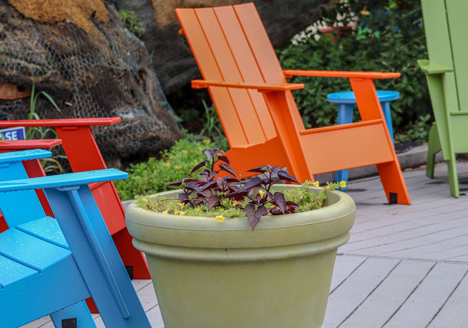 Colorful red, blue, orange, and green Adirondack chairs arranged on a deck next to a potted planter