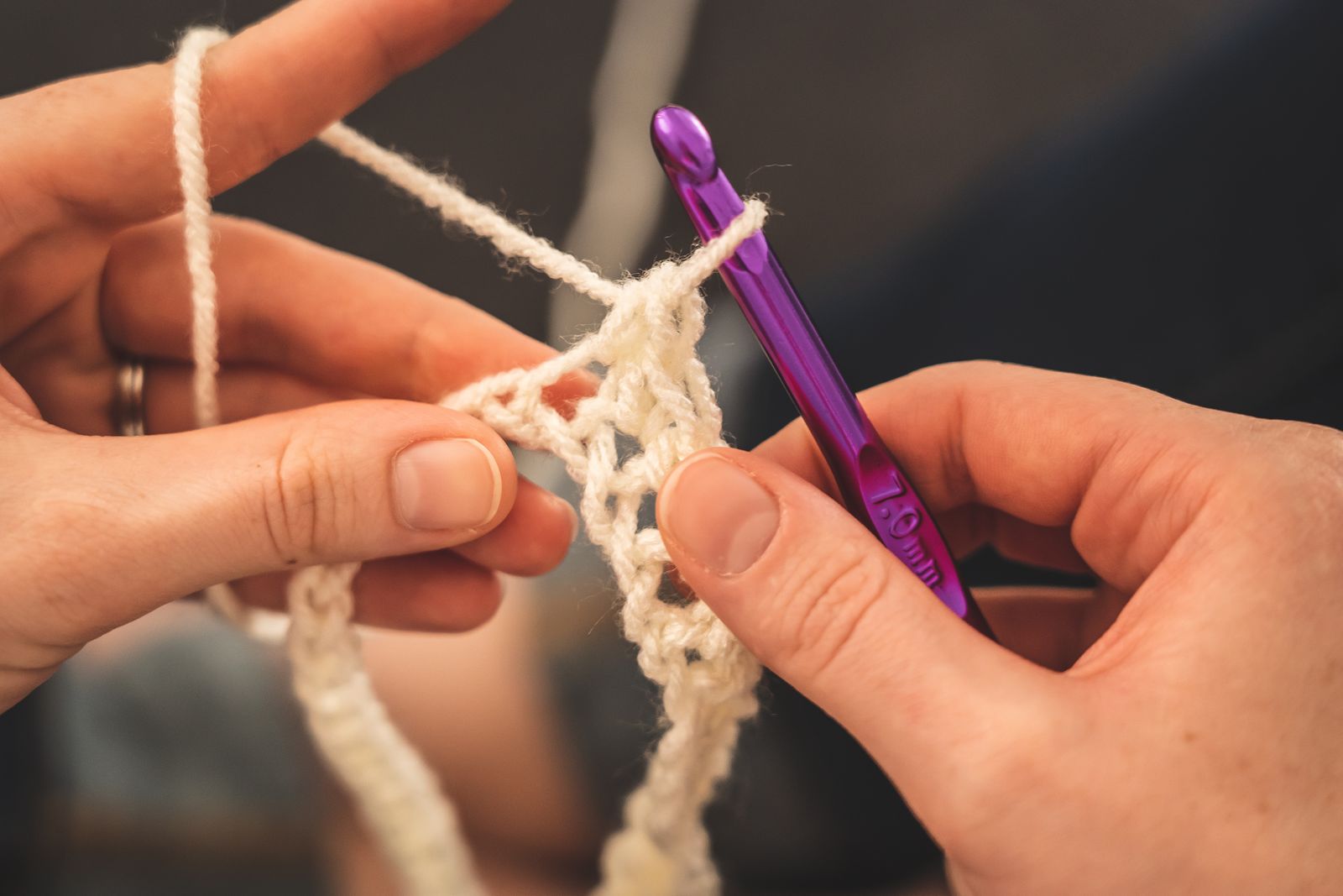 Close-up of a person's hands holding a crochet hook and working white yarn