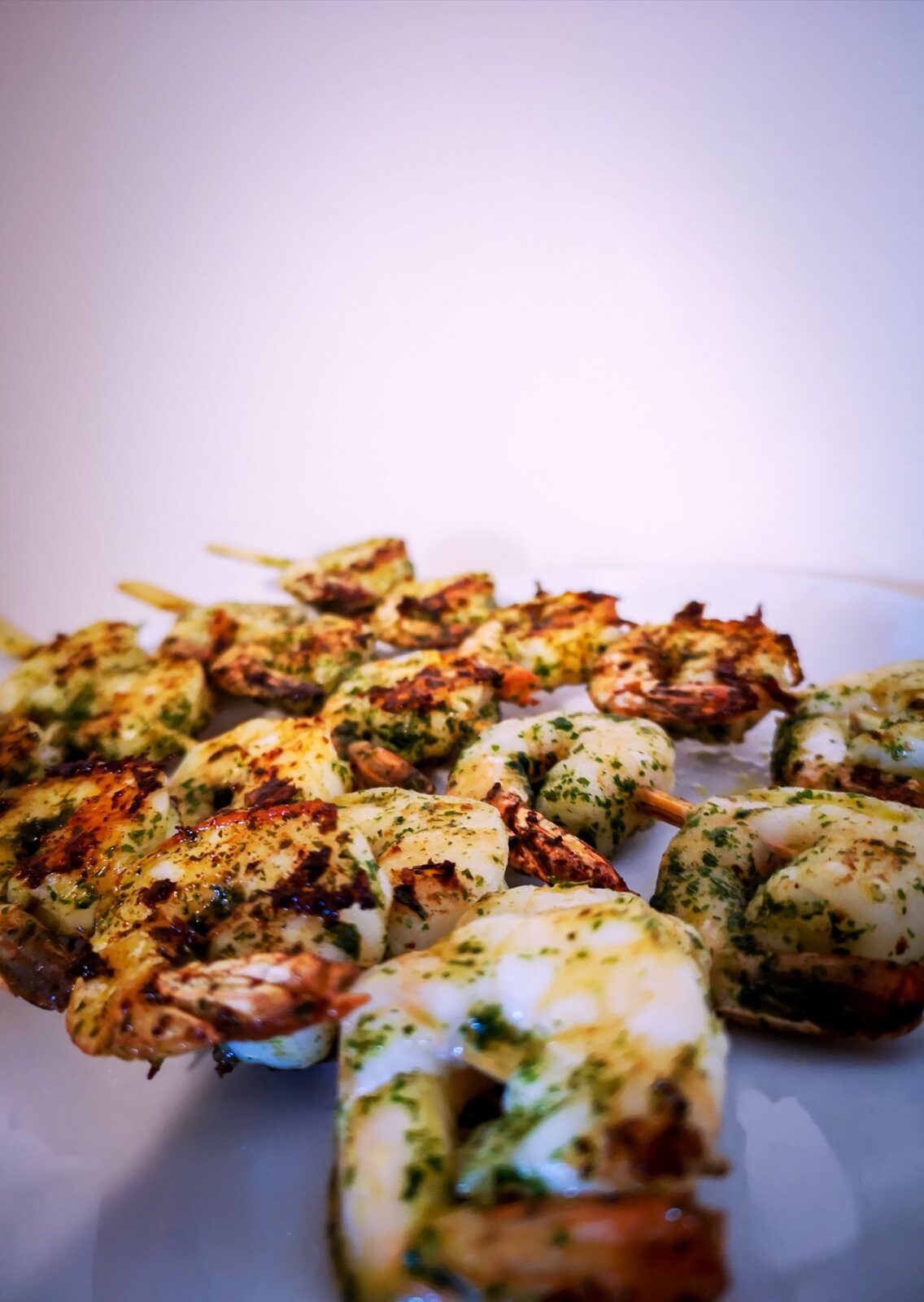 Grilled shrimp skewers glazed with herbs on a white plate