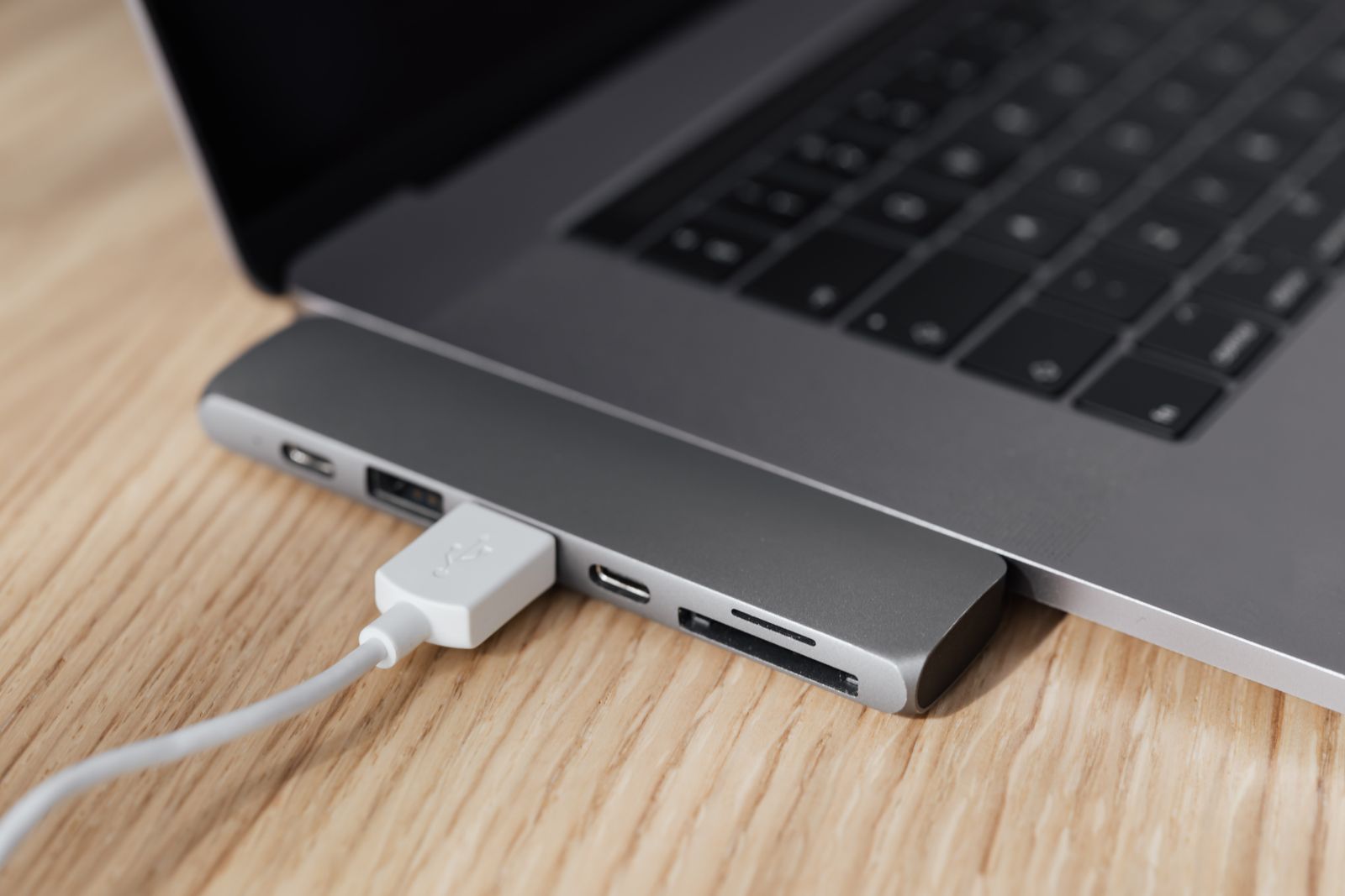 A USB-C docking station hub plugged into a silver laptop on a desk