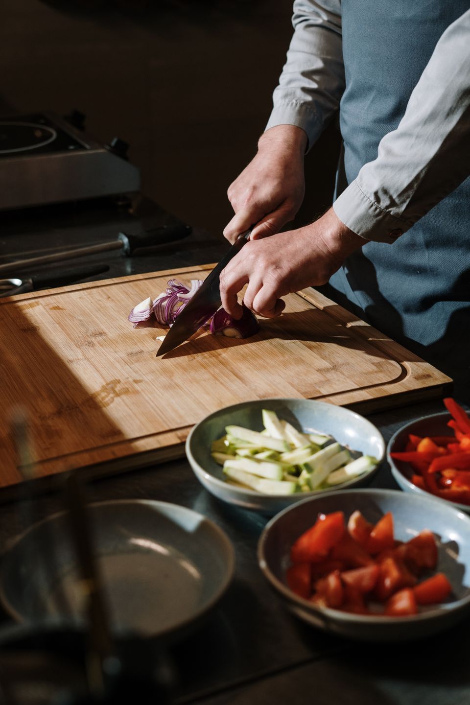 A cook slicing vegetables on a wooden board next to bowls of peppers and zucchini
