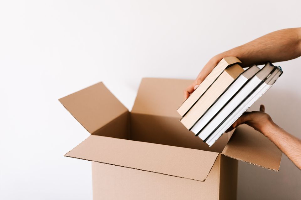 Close-up of hands placing stacked books into an open cardboard box