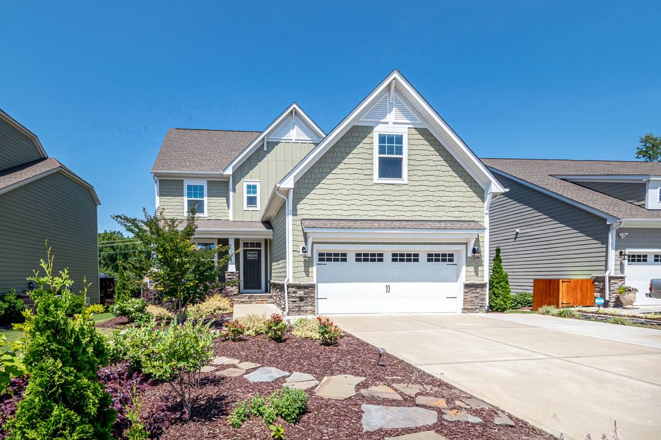 Two-story suburban house with a dark garage door and a driveway, photographed on a clear day
