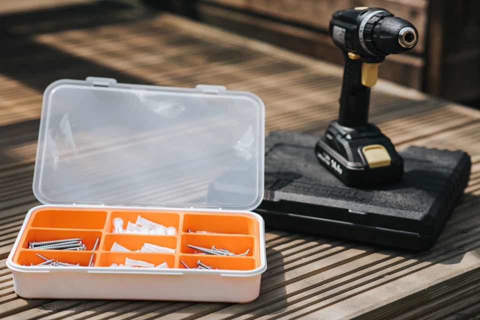 Open toolbox with screws and a cordless drill laid out on a wood deck