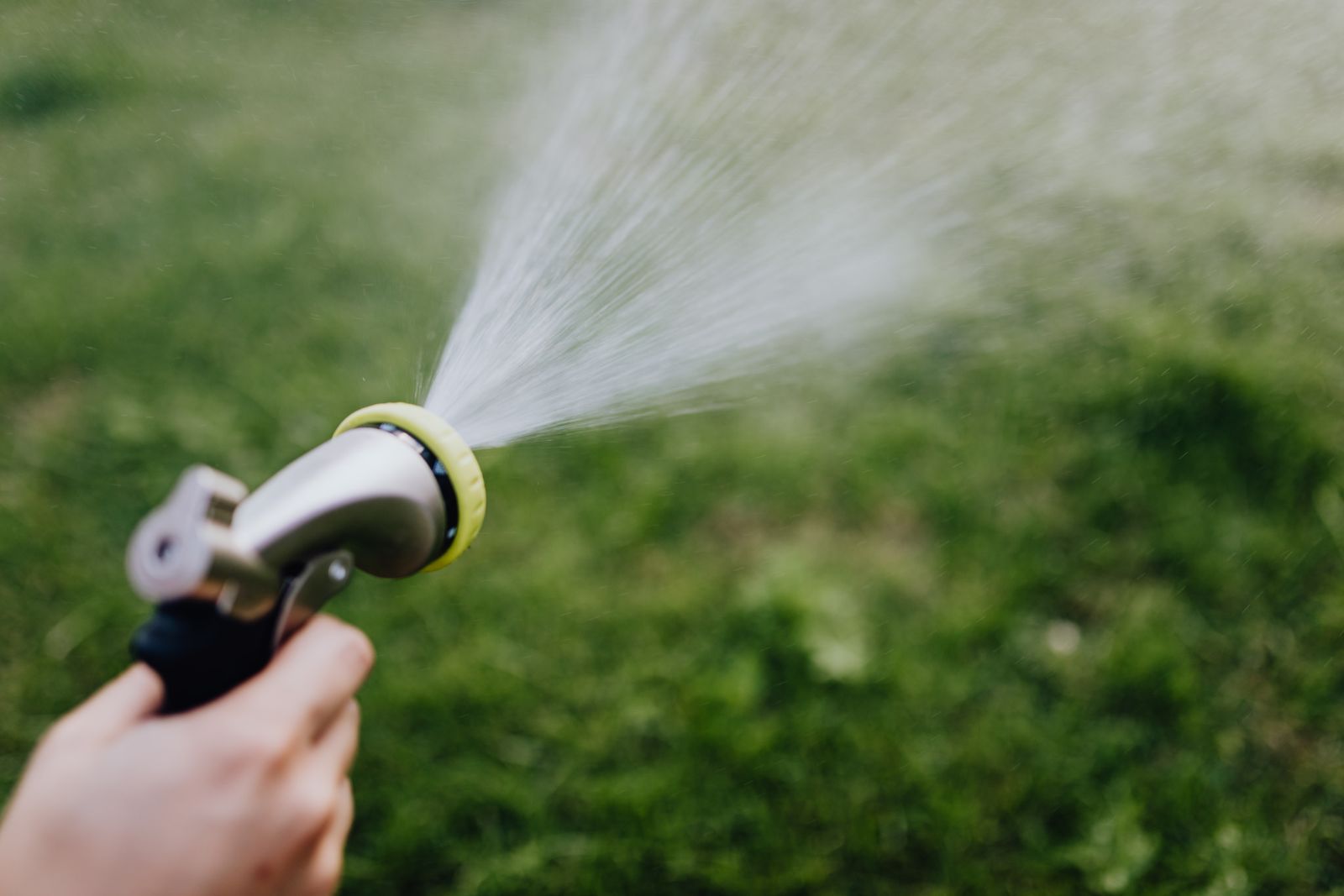Close-up of a garden hose nozzle spraying water over green grass