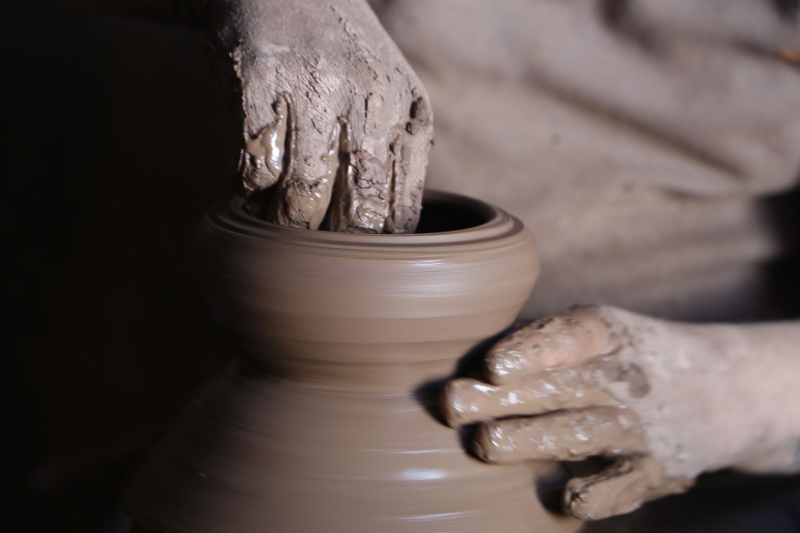 A potter's muddy hands guiding clay into shape as a pottery wheel spins