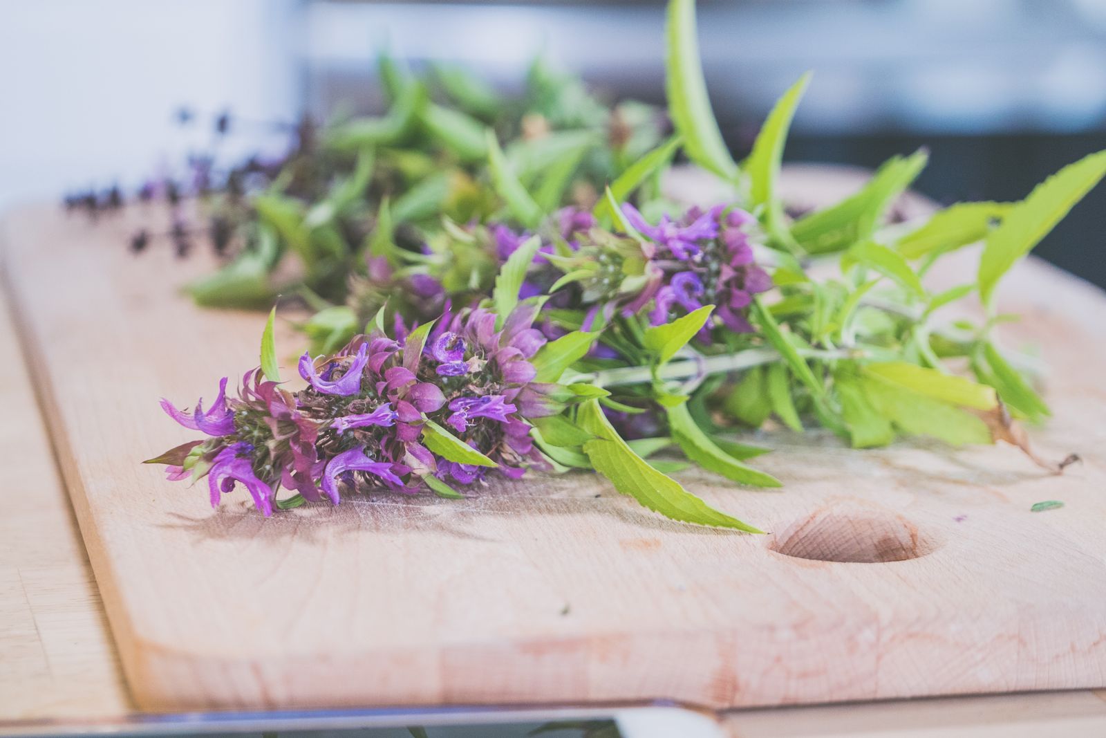 A bunch of fresh herbs with stems lying on a wooden cutting board