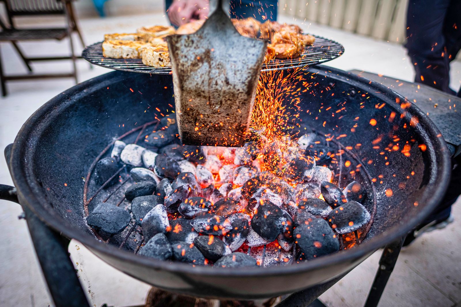 A round charcoal grill with hot glowing coals and sparks from a metal spatula