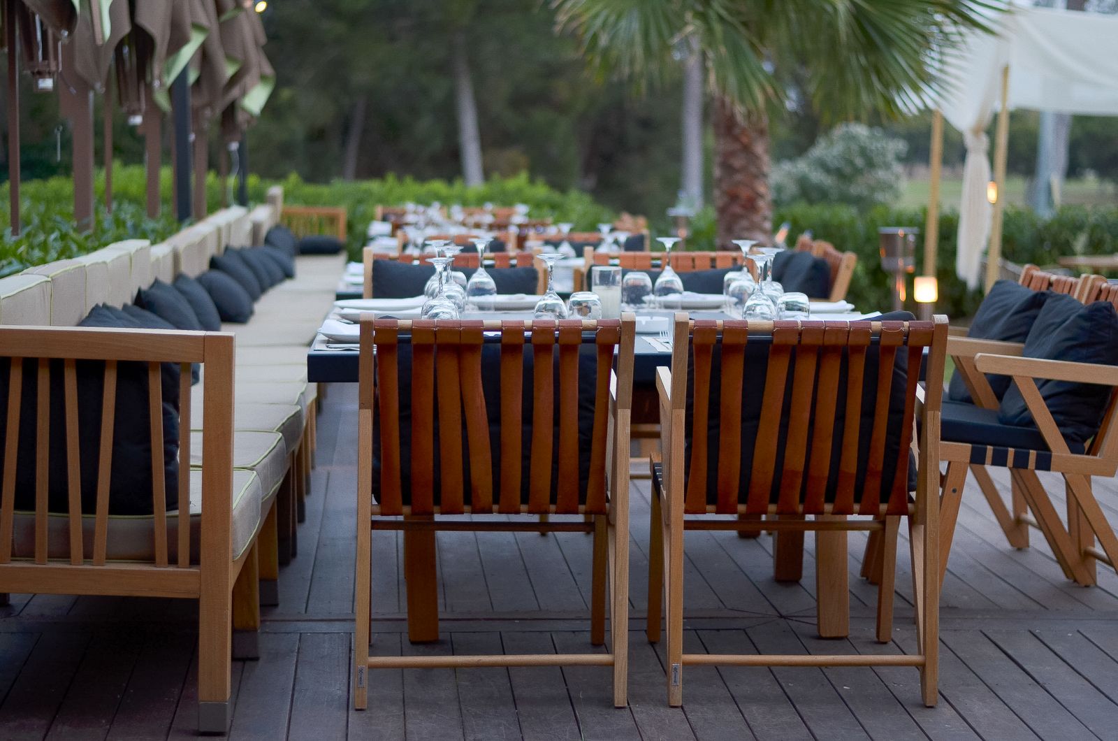 Wooden outdoor dining tables and chairs arranged on a shaded patio terrace