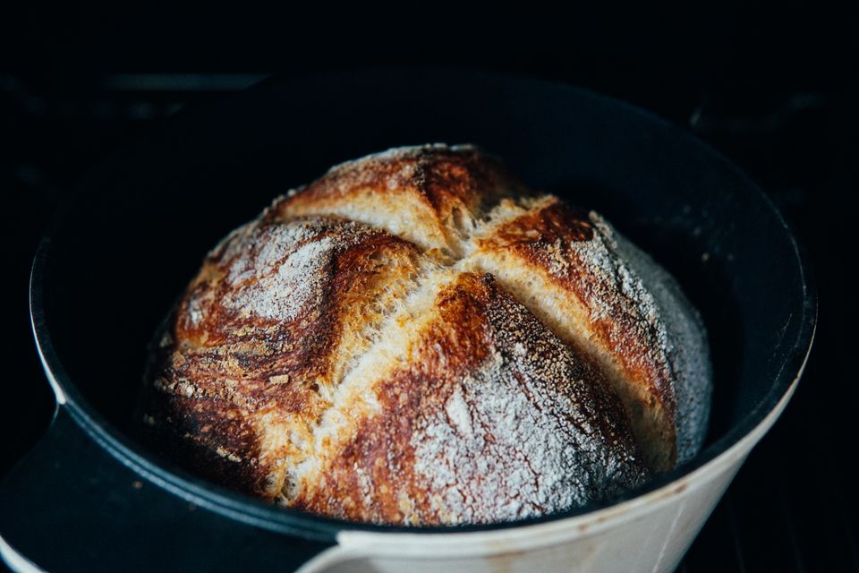 A golden baked bread loaf resting beside an open cast iron baking pot
