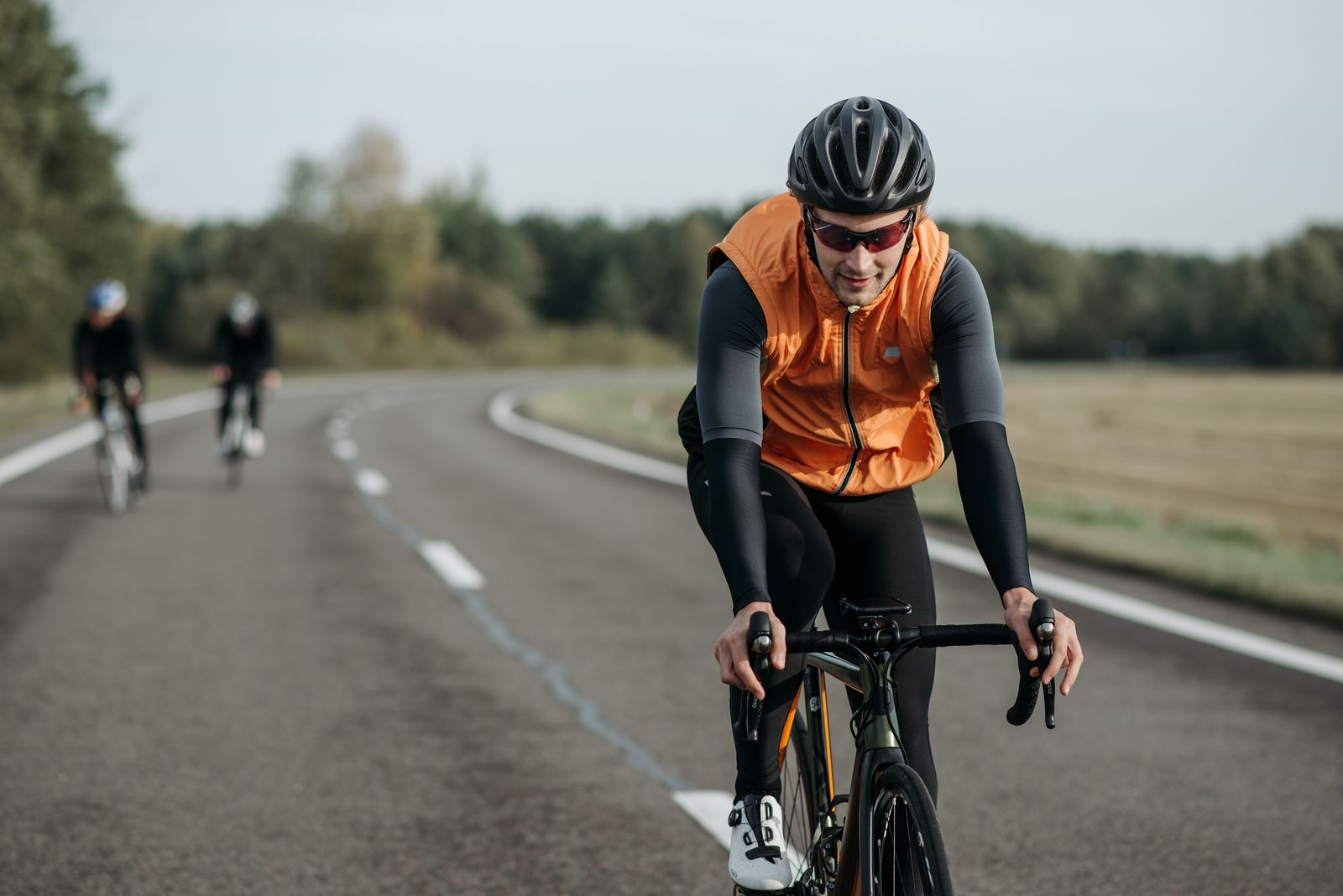 Close-up shot of three cyclists in activewear riding bikes together along a paved country road