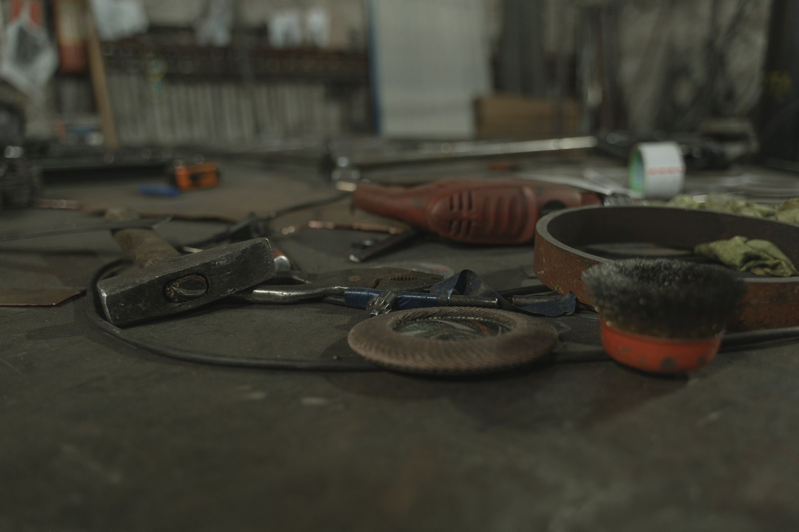 Workbench cluttered with a hammer, pliers, cordless power tool, grinding disc, and wire brush in a workshop