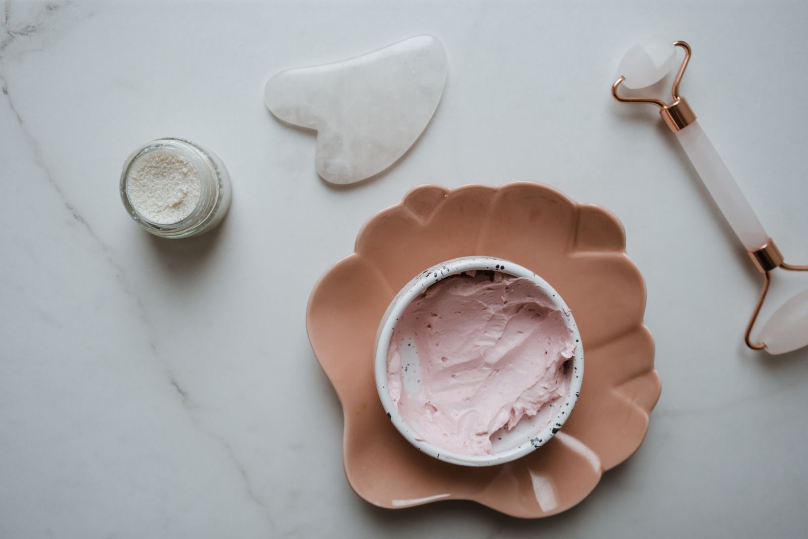 Flat lay of a gua sha stone tool and jade facial roller on a marble surface for a skincare routine