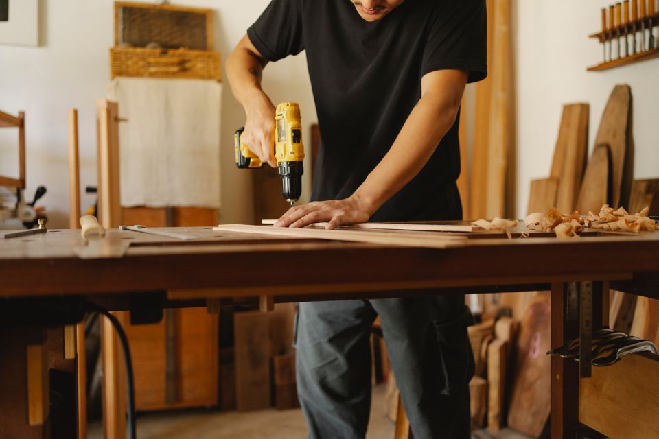 Person using a cordless drill on a wooden plank in a workshop