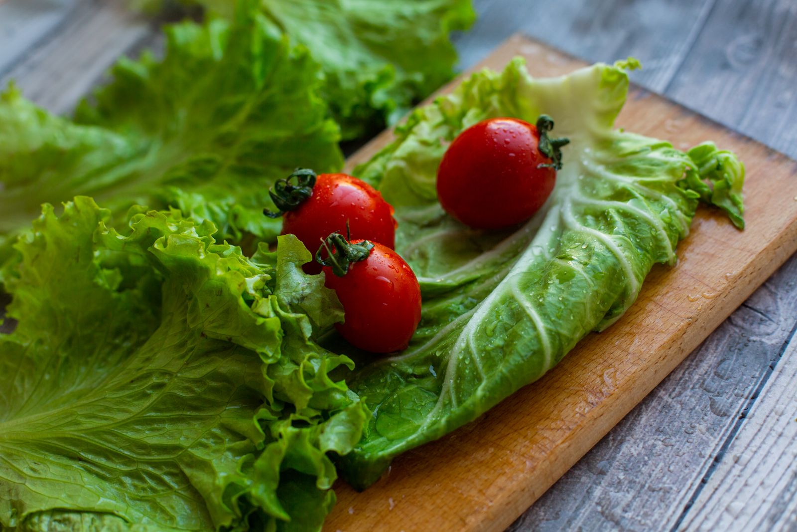 Wet lettuce leaves and cherry tomatoes on a wooden cutting board after washing