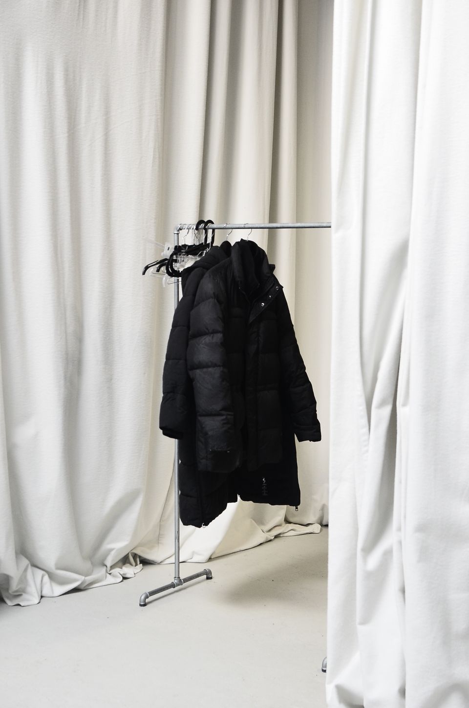 Black coats and jackets hung on a simple metal hook rack against a bright wall