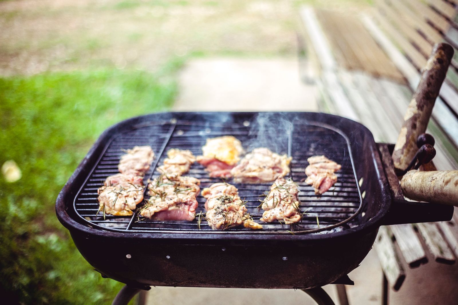Grill smoking on a backyard patio next to a wooden bench and lawn