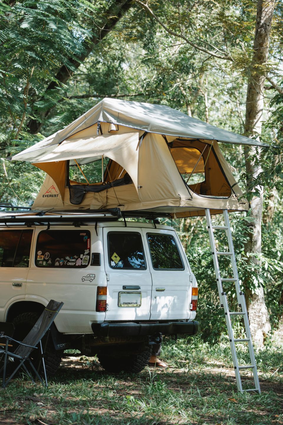 White SUV with a rooftop tent parked among trees on a camping road trip