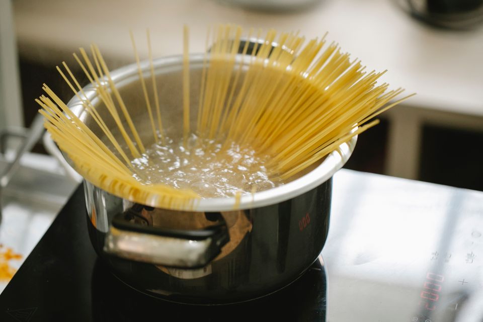 Uncooked spaghetti noodles in a stainless steel pot of boiling water on a stove