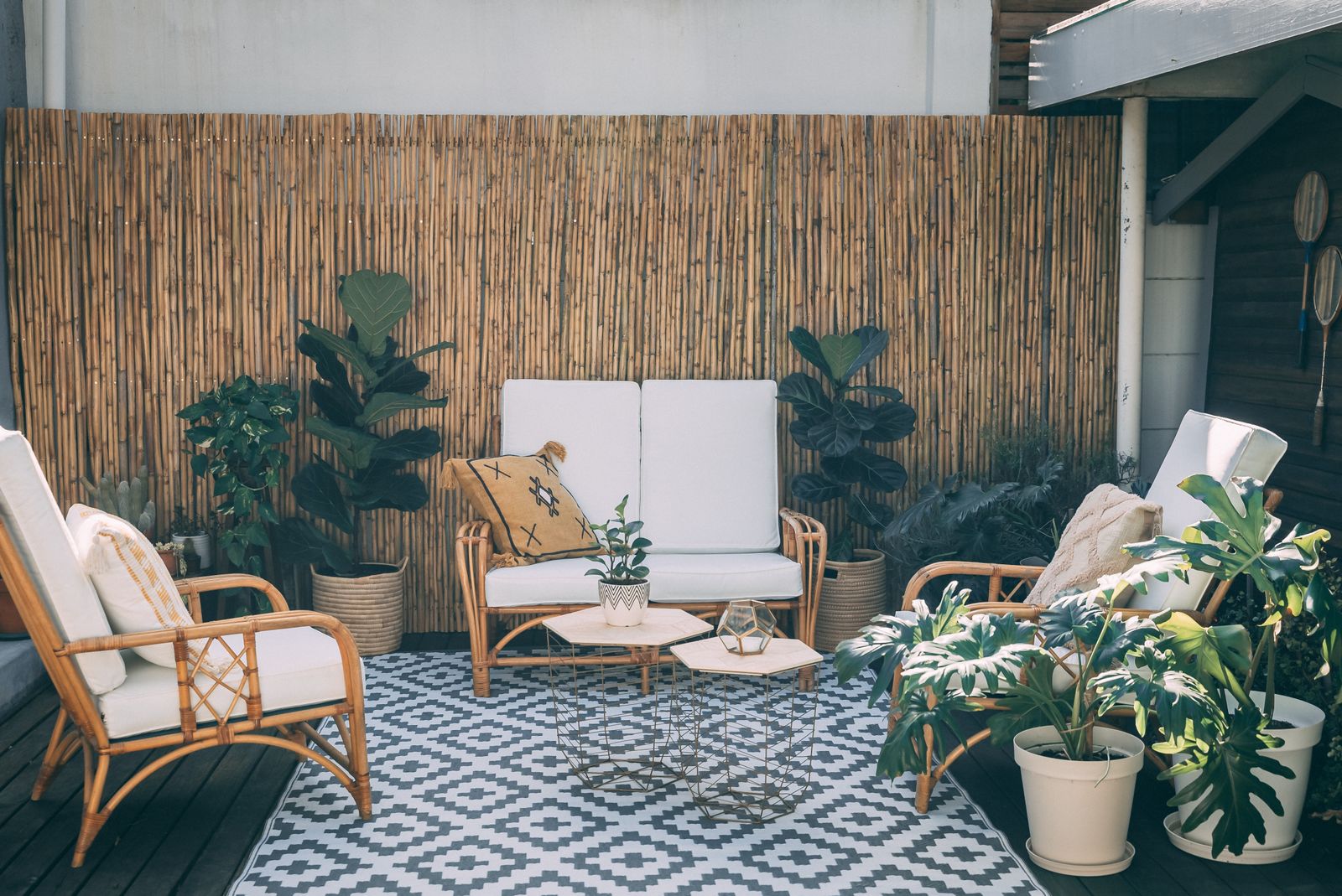 Outdoor patio with a woven rug beneath rattan seating, potted plants, and bamboo decor
