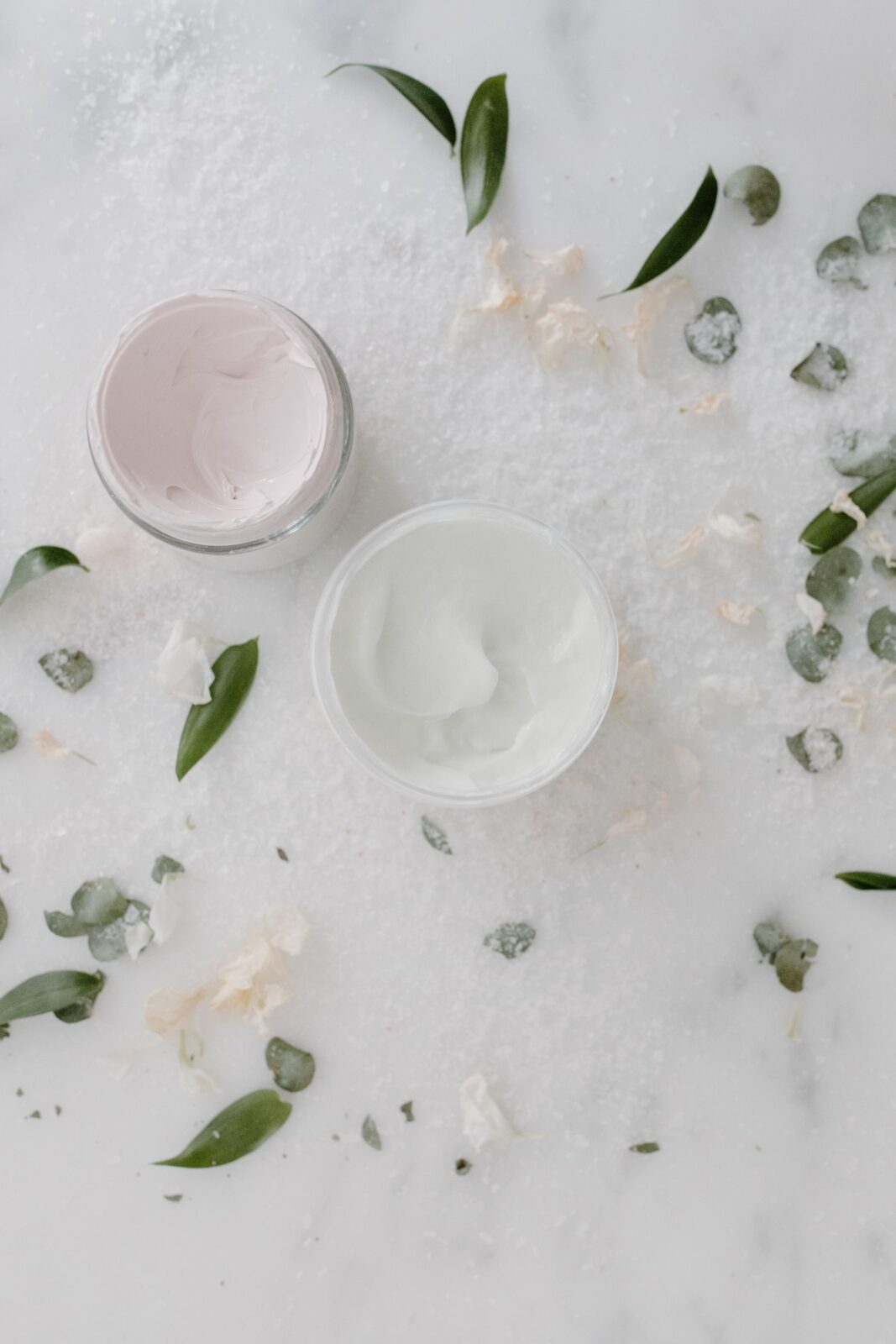 Two open glass jars of face moisturizer cream on a marble surface