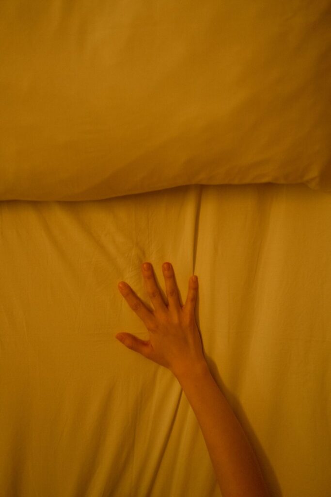 A hand gently touching a bed sheet in warm morning light