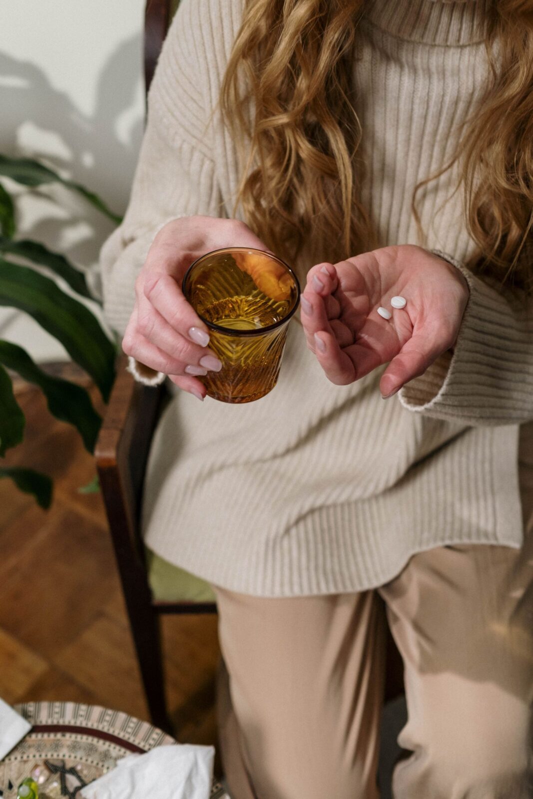 Woman seated indoors holding a dose of pills in one hand and a glass of water in the other