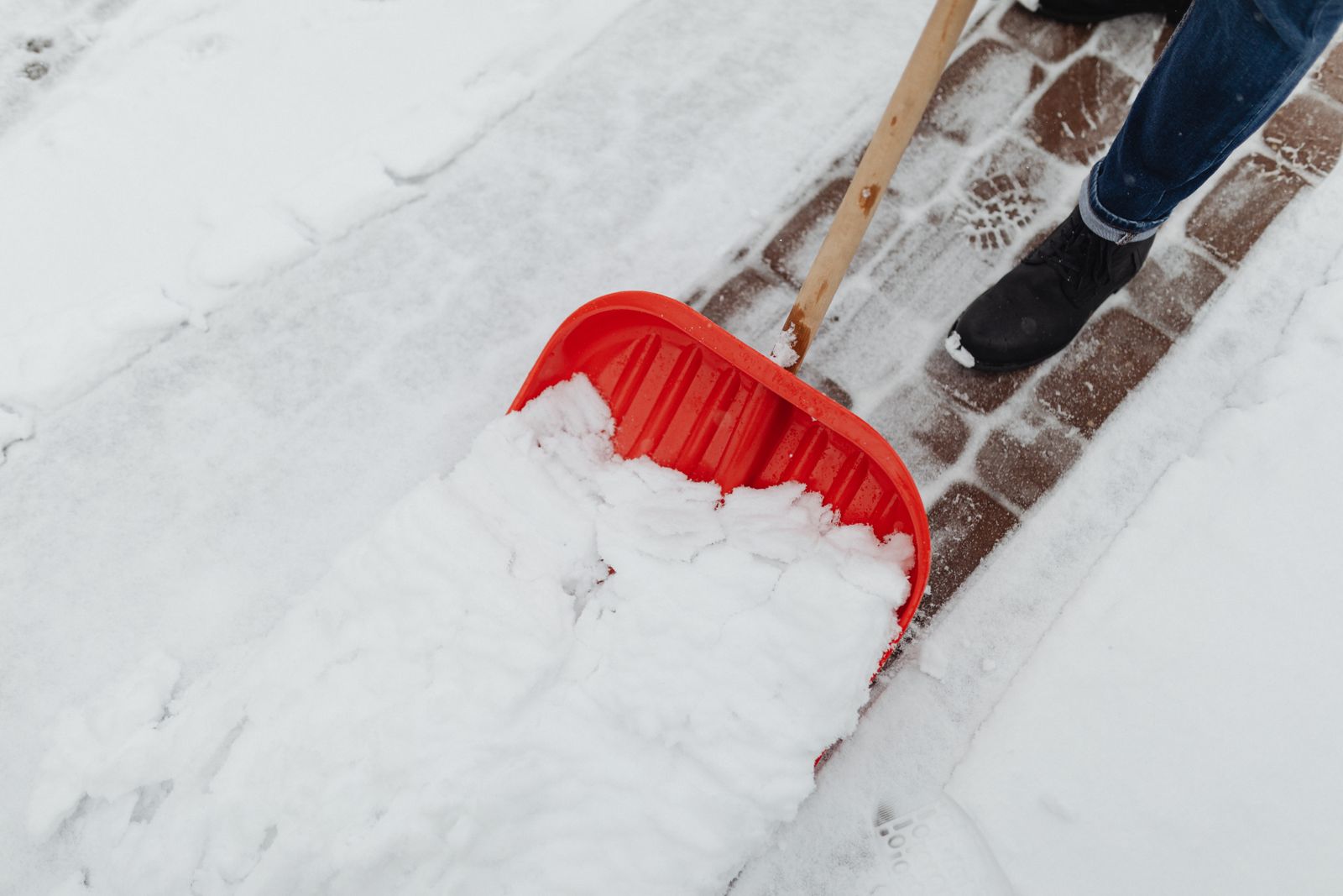 Close-up of a person using a red snow shovel to clear a driveway