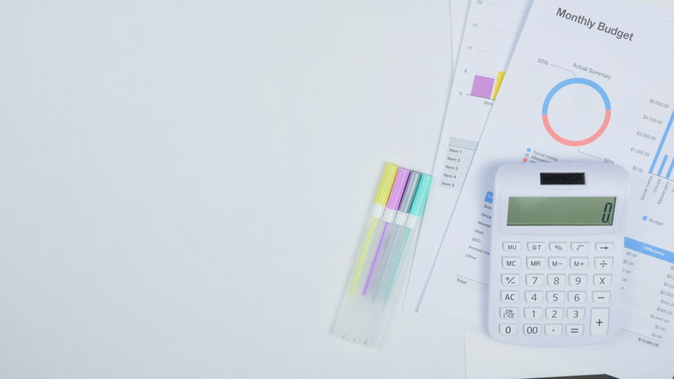 Minimalist desk with a calculator, budget planning documents, and colorful pens