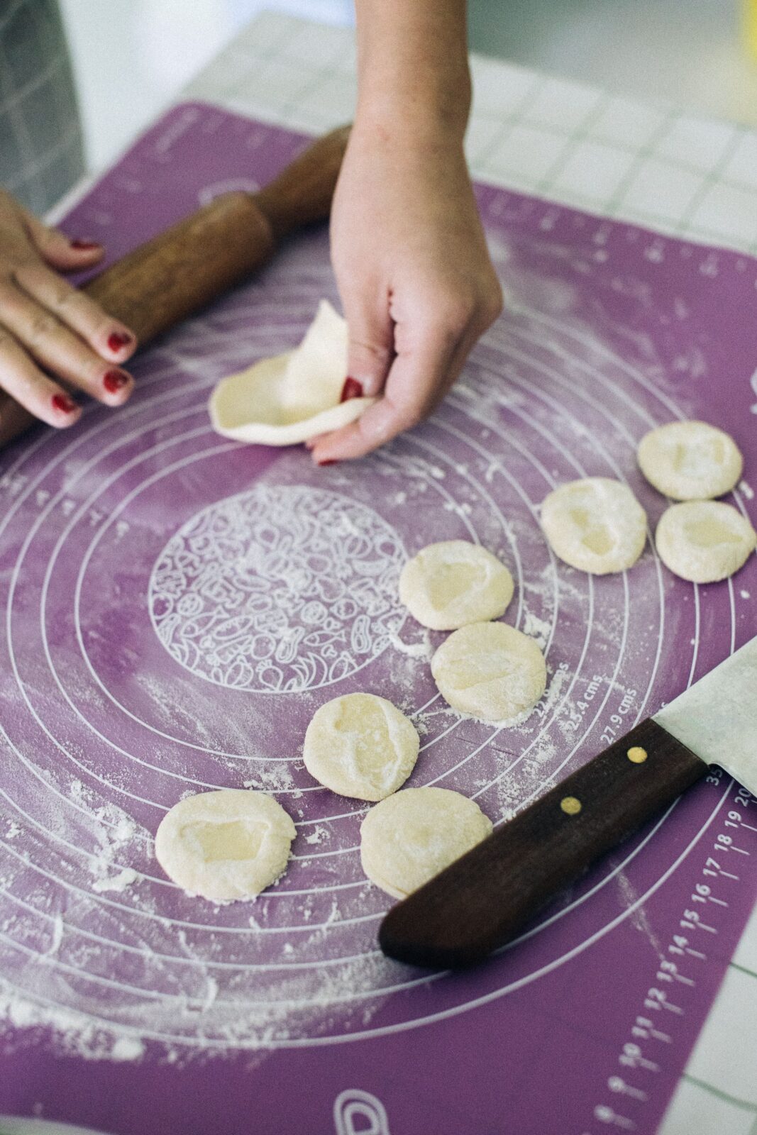 A knife and a rolling pin resting on a printed silicone mat beside rounds of dough