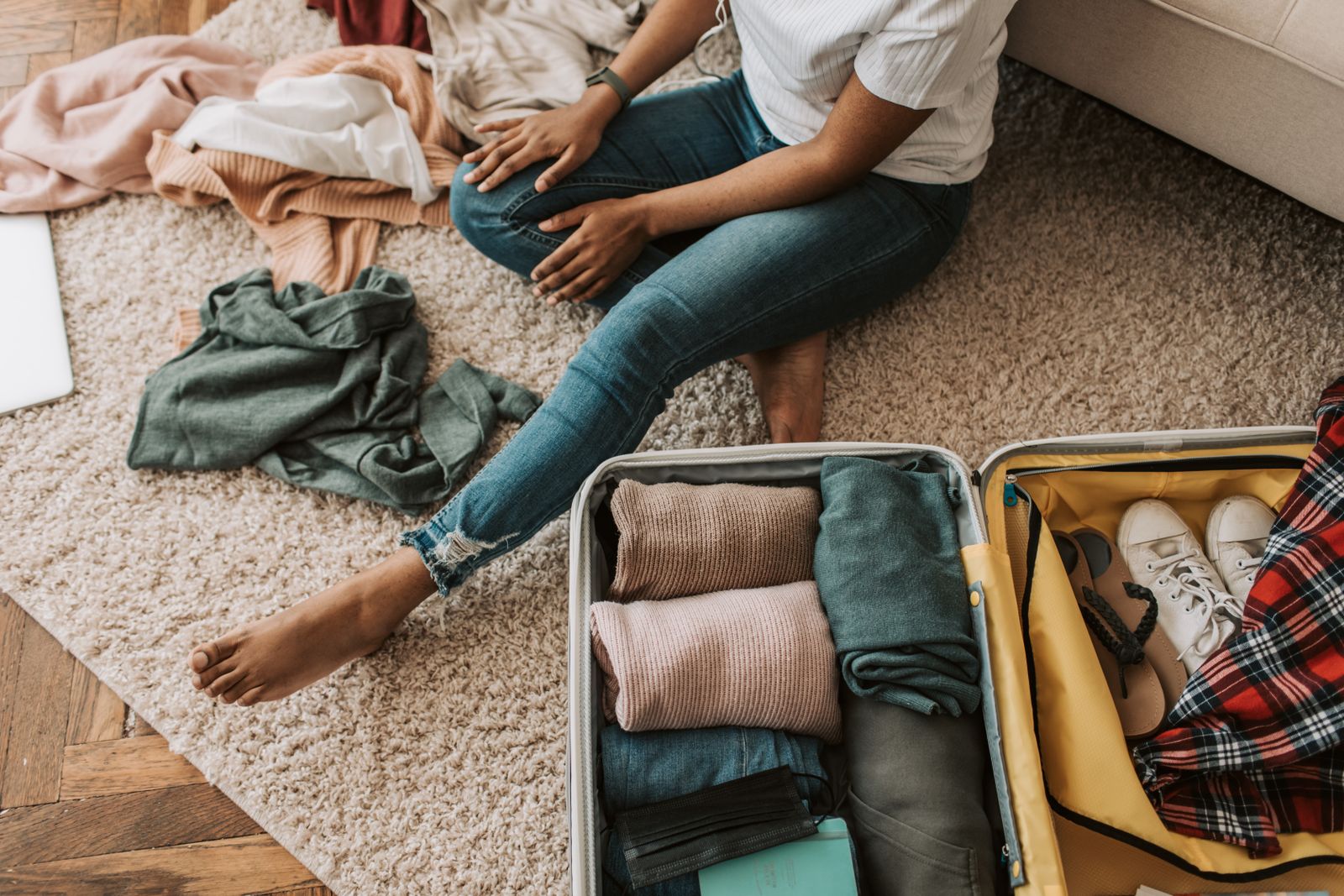 A traveler sitting on the floor sorting folded clothes into piles next to an open suitcase