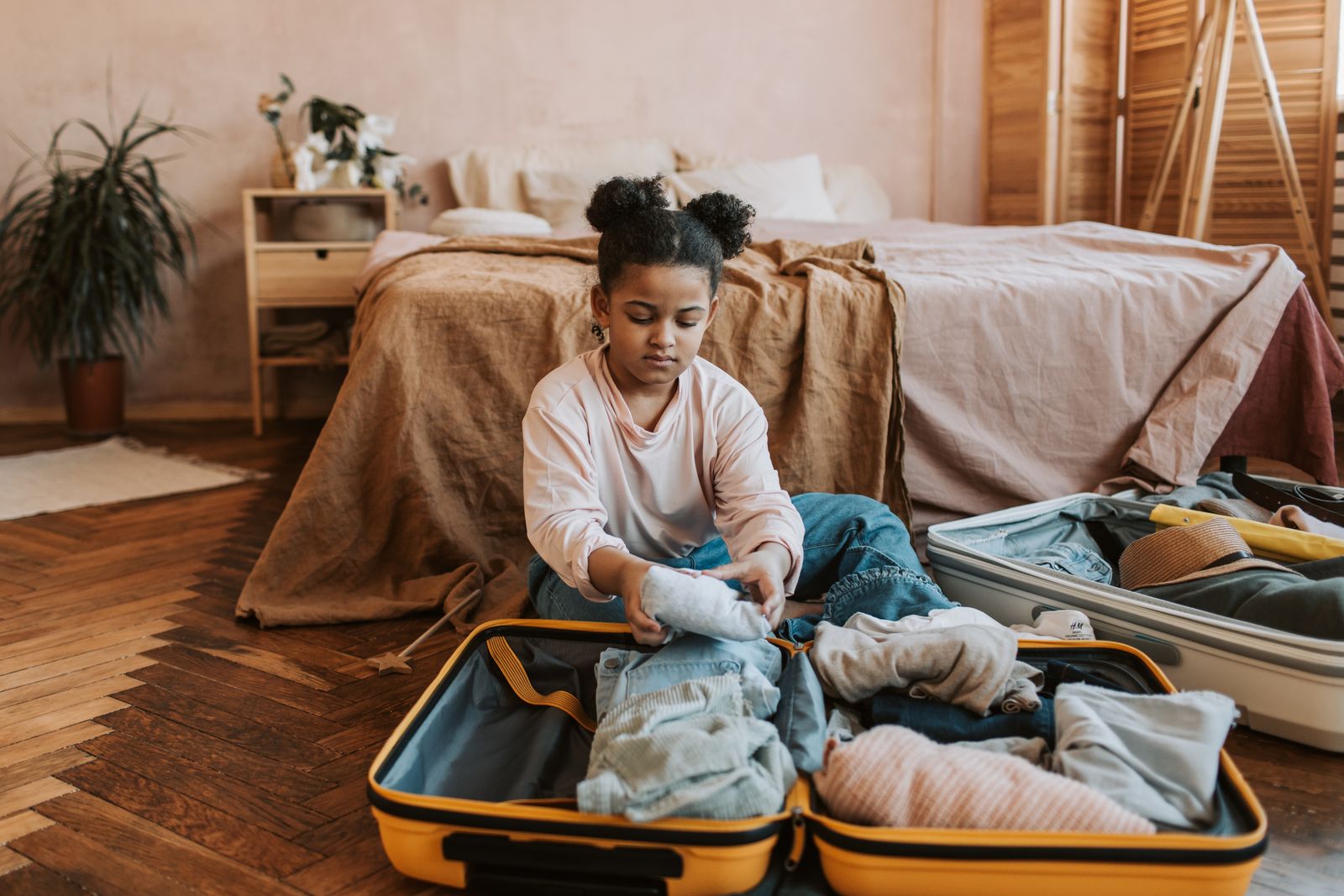 A woman sitting on the edge of a bed with an open suitcase in front of her, packing for a trip