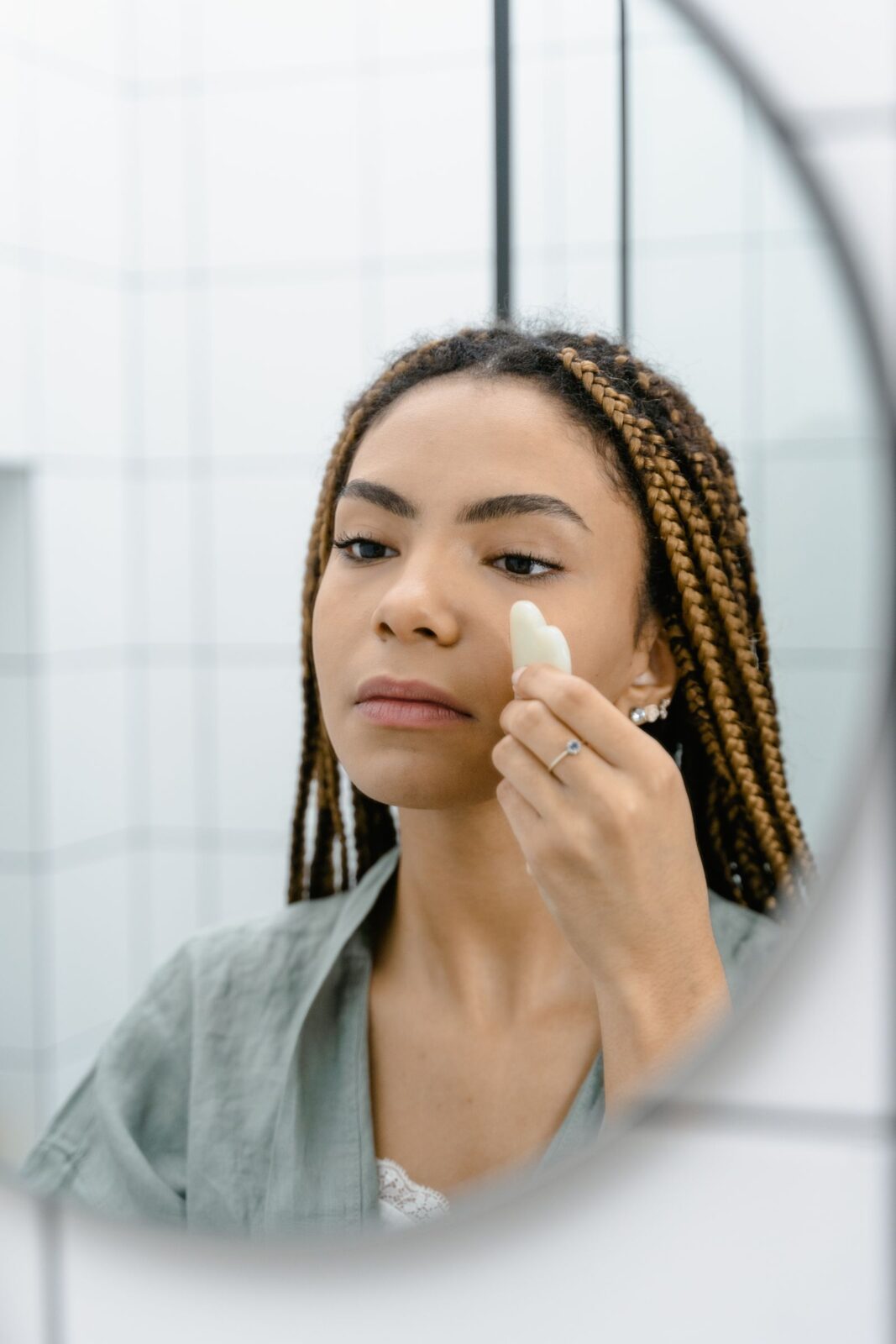 Woman using a gua sha tool along her jawline in front of a mirror as part of a skincare routine