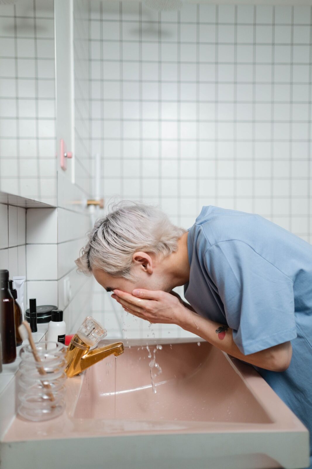 Person washing their face at a bathroom sink with a few unlabeled skincare products nearby