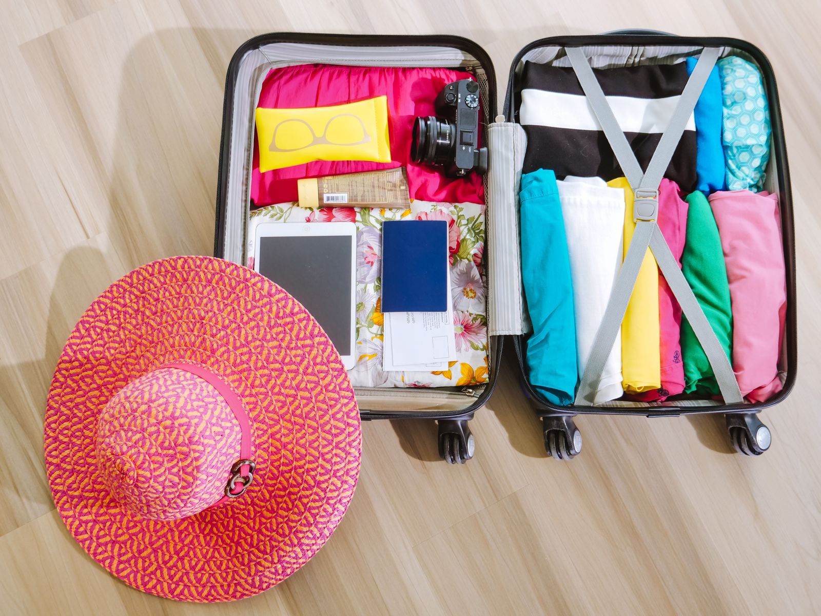 An open suitcase packed for a trip with clothes, sunglasses, a camera, and a tablet arranged neatly