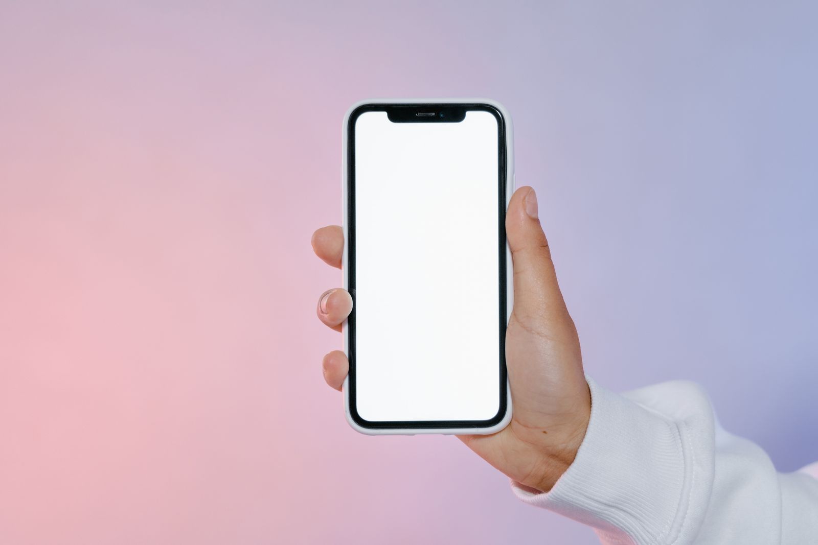 Hand holding a smartphone with a blank screen against a soft pastel background