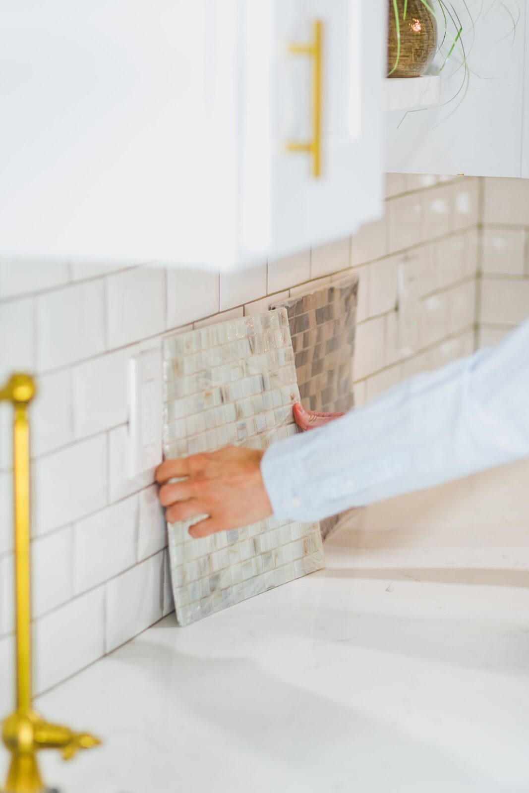 Person holding a sample of small mosaic tiles against an existing white subway tile kitchen backsplash