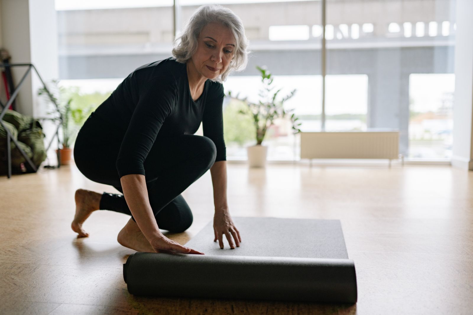 Woman in black leggings and long-sleeve top rolling out a yoga mat in a bright studio