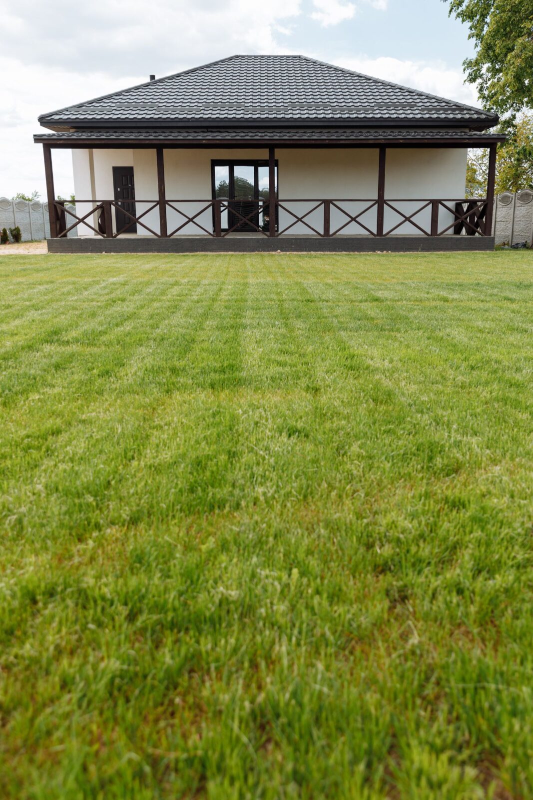 Small residential lawn with fresh mowing stripes in front of a house with a covered porch