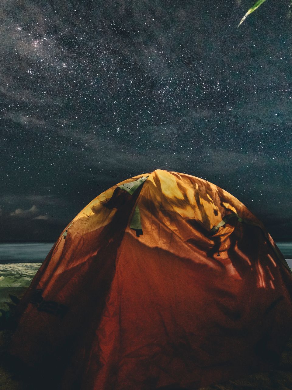 Illuminated camping tent under a starry night sky, the kind of dark campsite where a battery-powered projector performs best