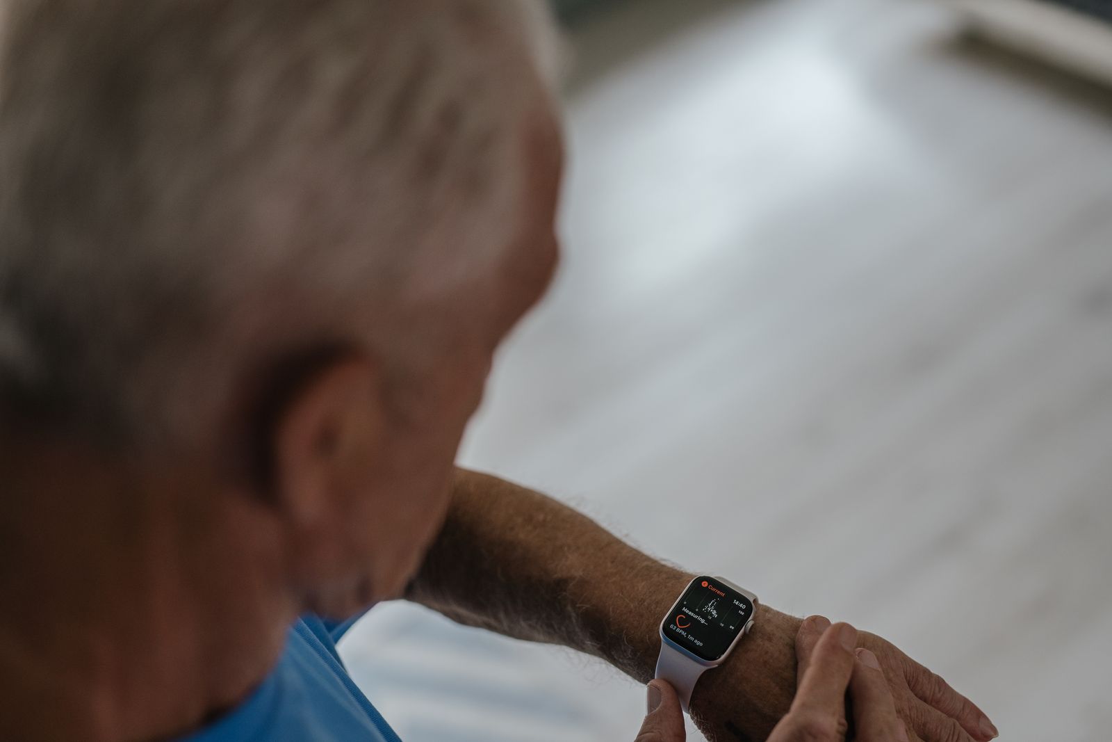 An older adult looking closely at a smartwatch on their wrist indoors