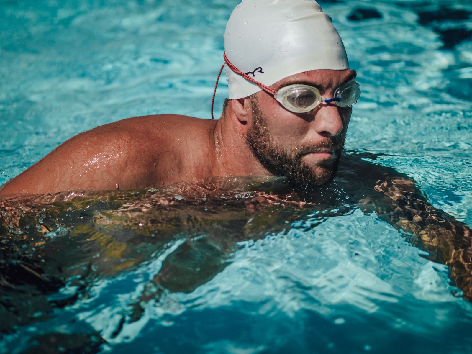 Swimmer mid-stroke in a pool wearing goggles and a swim cap