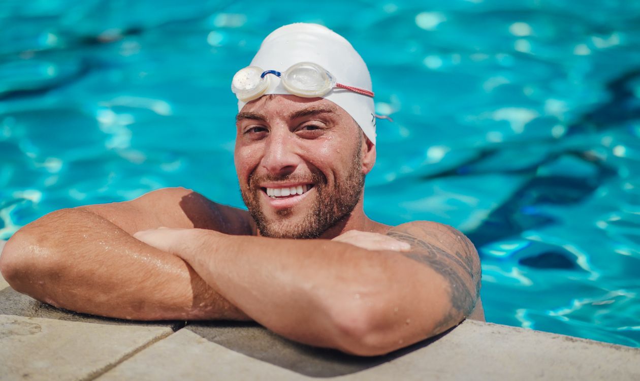 Swimmer wearing goggles and a swim cap resting at the poolside after a training set