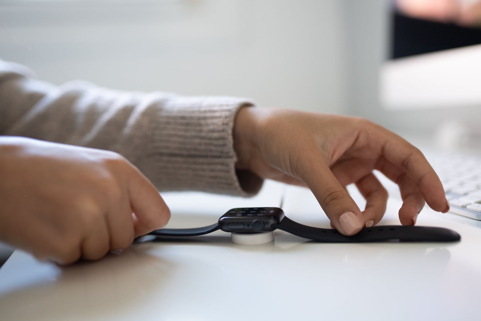 Close-up of hands placing a smartwatch on a charging dock on a white desk