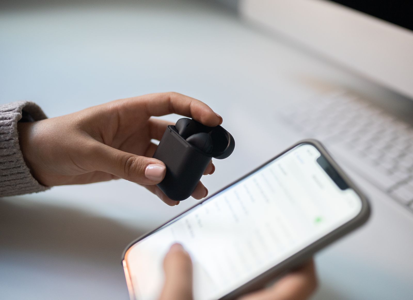 Close-up of hands holding wireless earbuds next to a smartphone screen