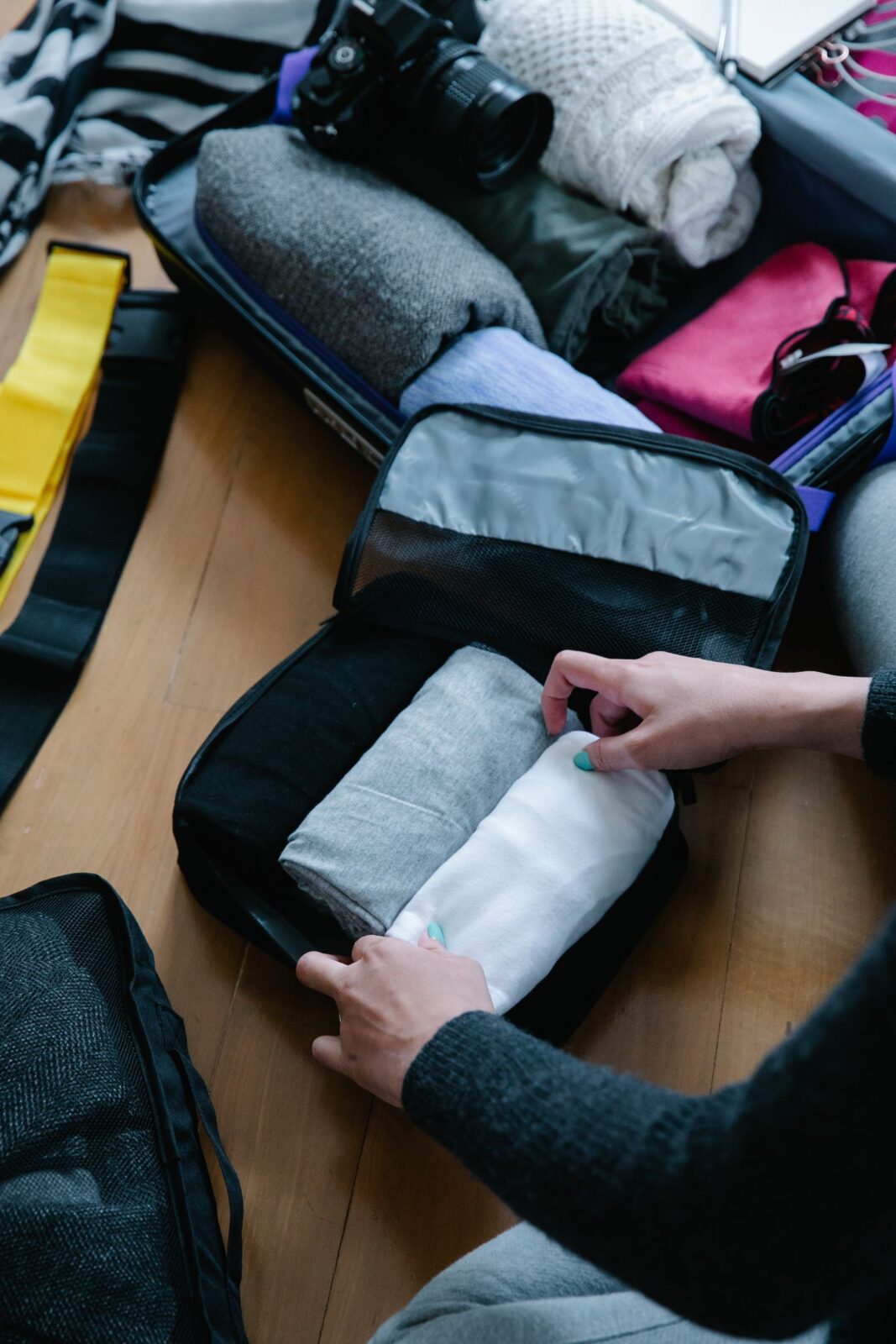 Close-up of hands folding a garment and placing it into a fabric packing cube next to a camera