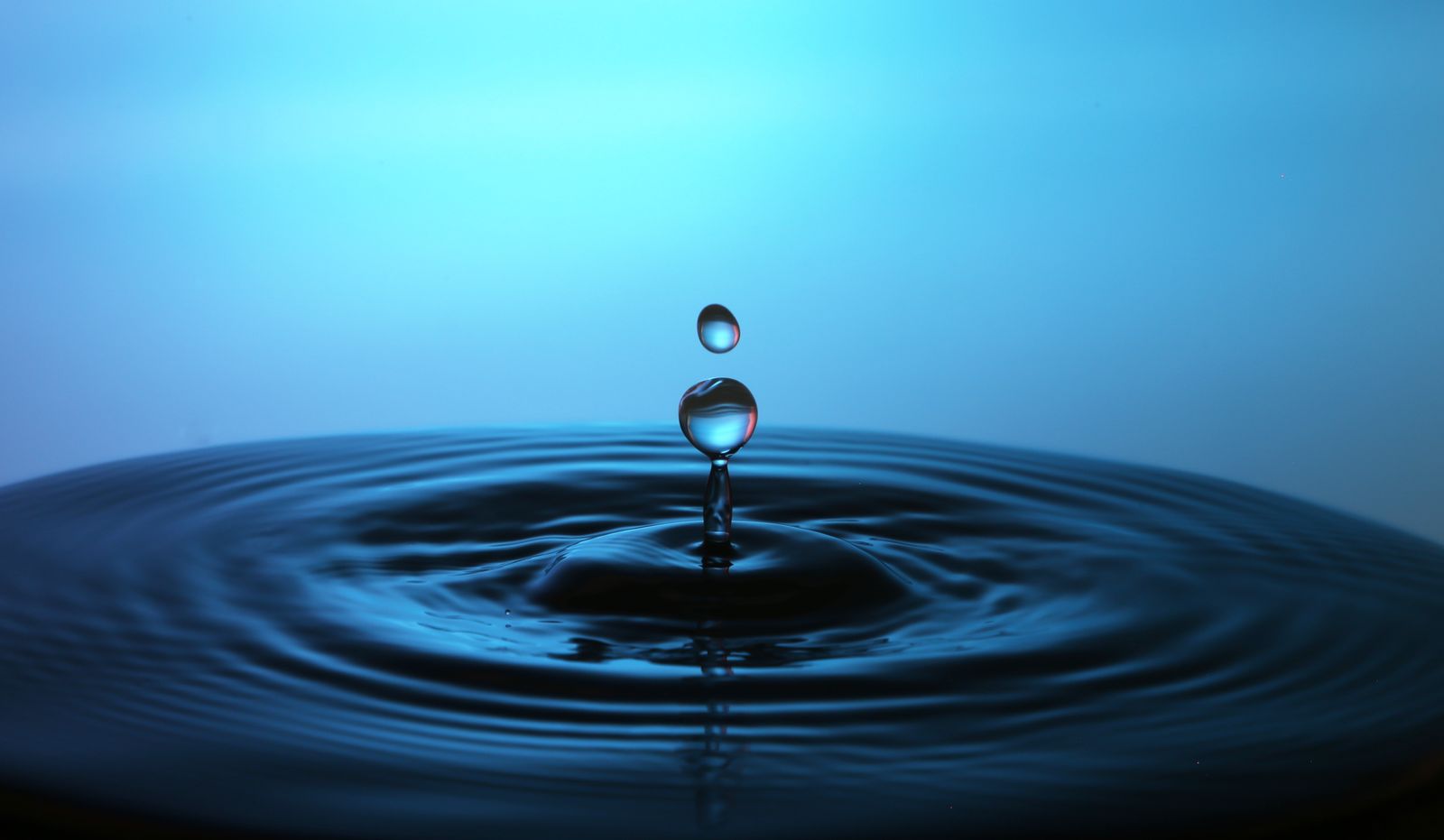 Macro close-up of a single water droplet creating ripples against a blue background