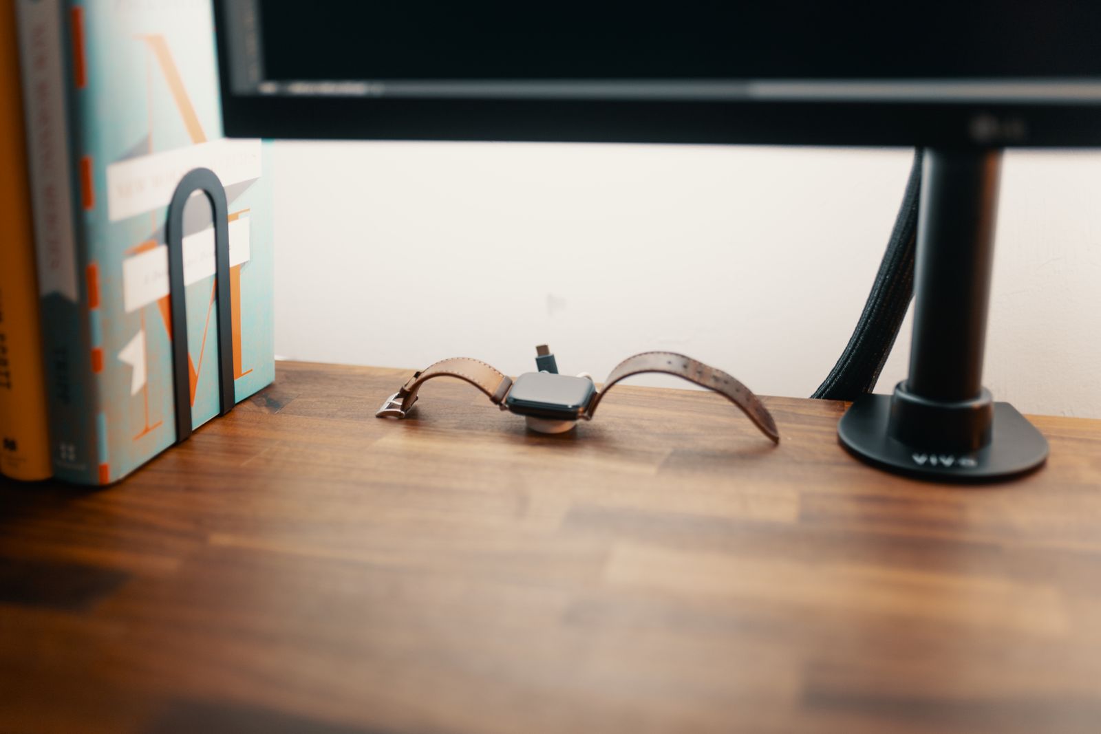 A smartwatch resting on its charger next to a stack of books on a nightstand