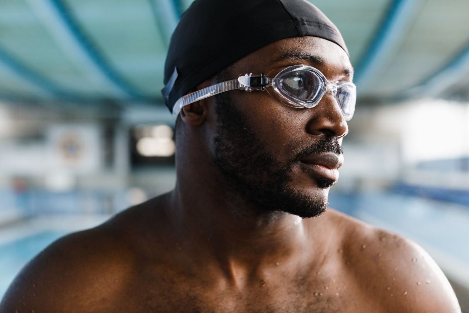 Swimmer wearing a dark swim cap and clear goggles pausing poolside after a training set