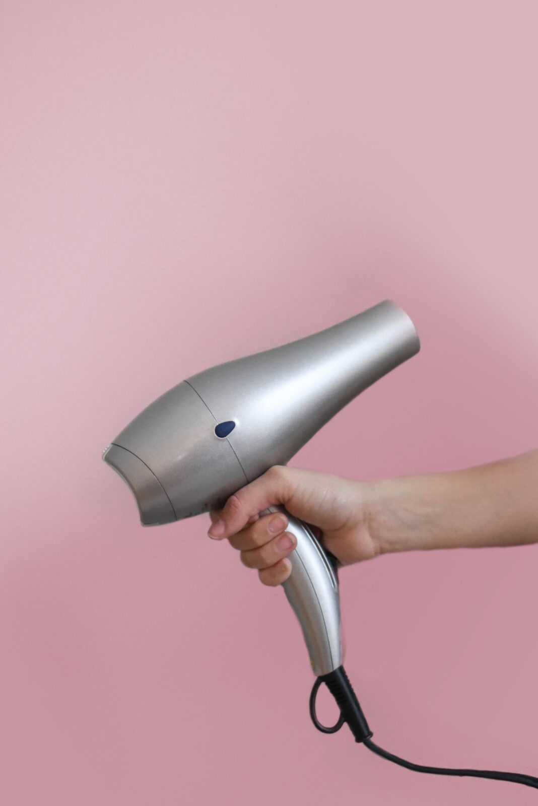 Close-up of a hand holding a handheld hair dryer, showing the nozzle end where diffuser attachments snap on